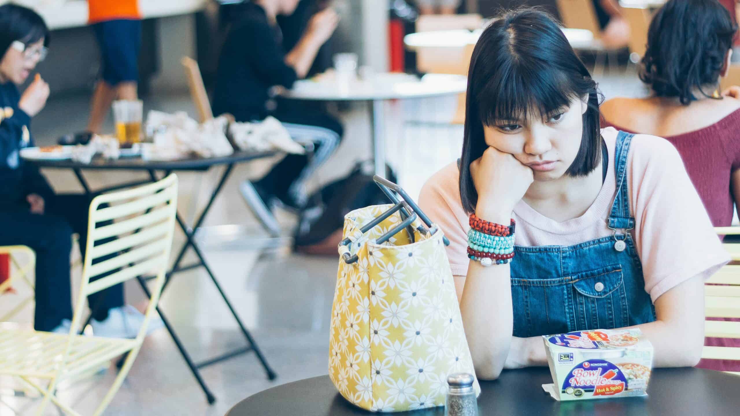 student sitting in college canteen thinking about the disadvantages of going to college