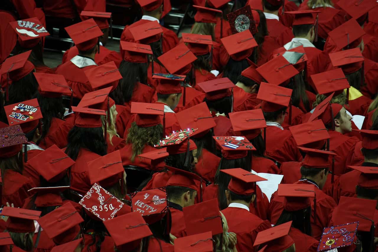 A large group of students dressed in red graduation caps and gowns seated at a commencement ceremony.
