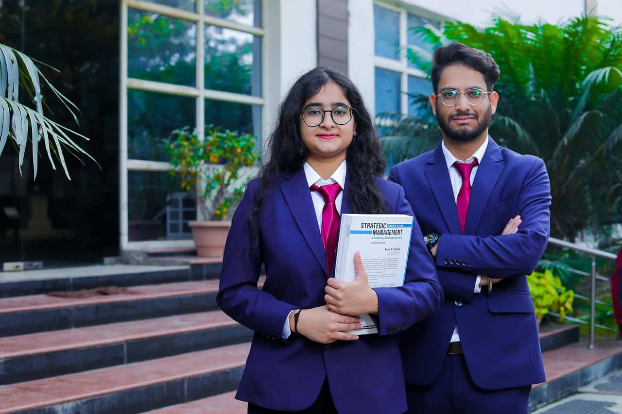Two confident students standing outside a college building, holding textbooks and ready to start their academic journey.